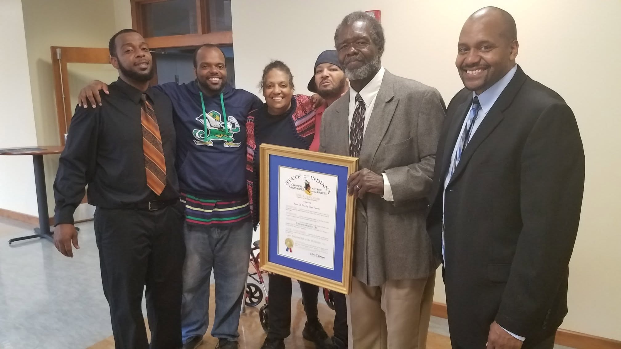 Family and community members gathered around a framed award