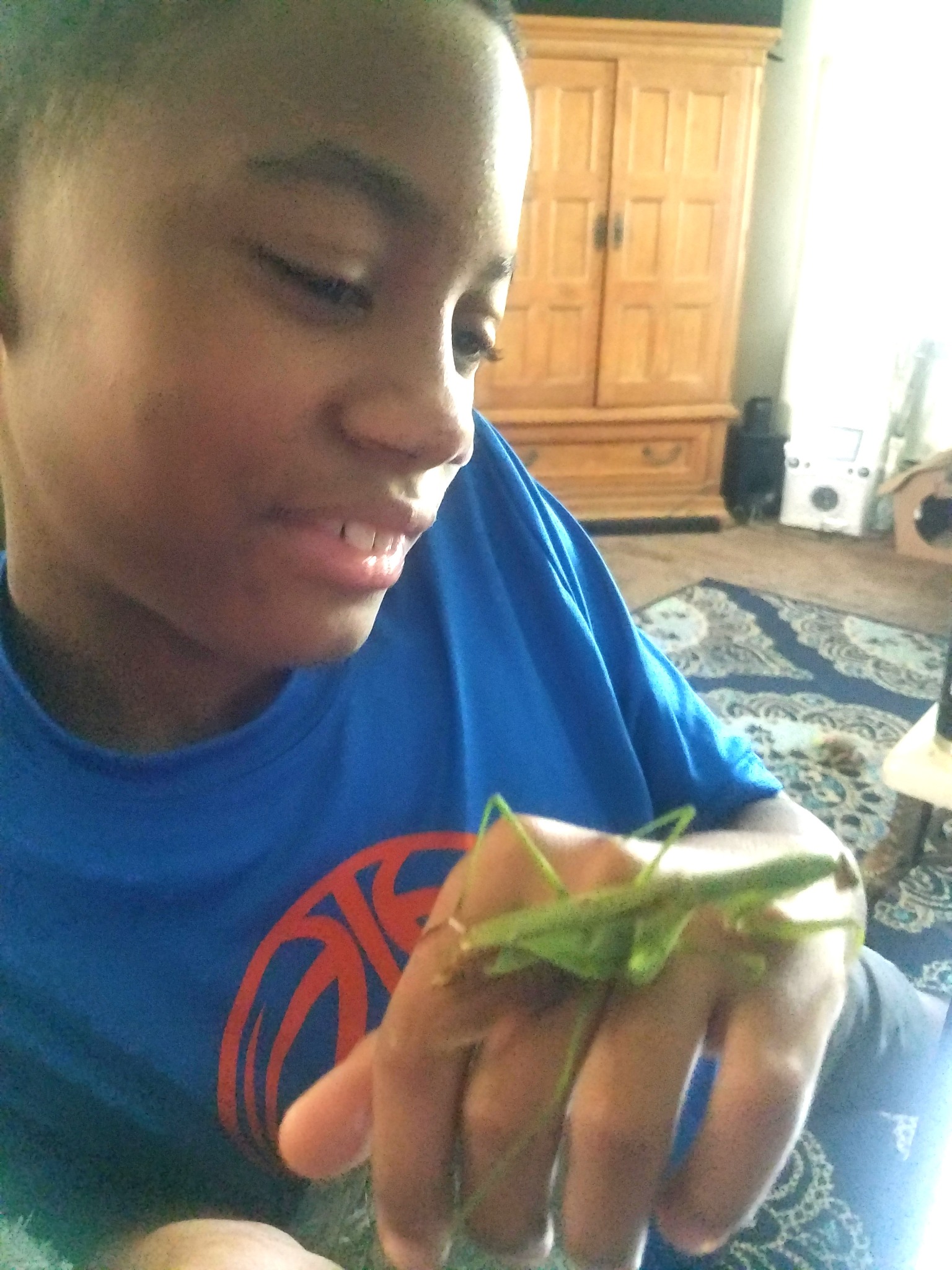 Jelani smiling with fascination at a green praying mantis resting on his hand