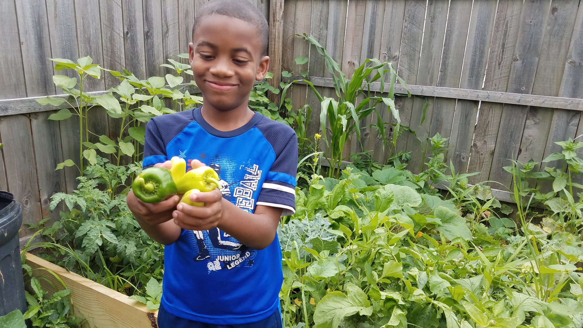 Jelani smiling proudly as he holds freshly harvested peppers in his garden